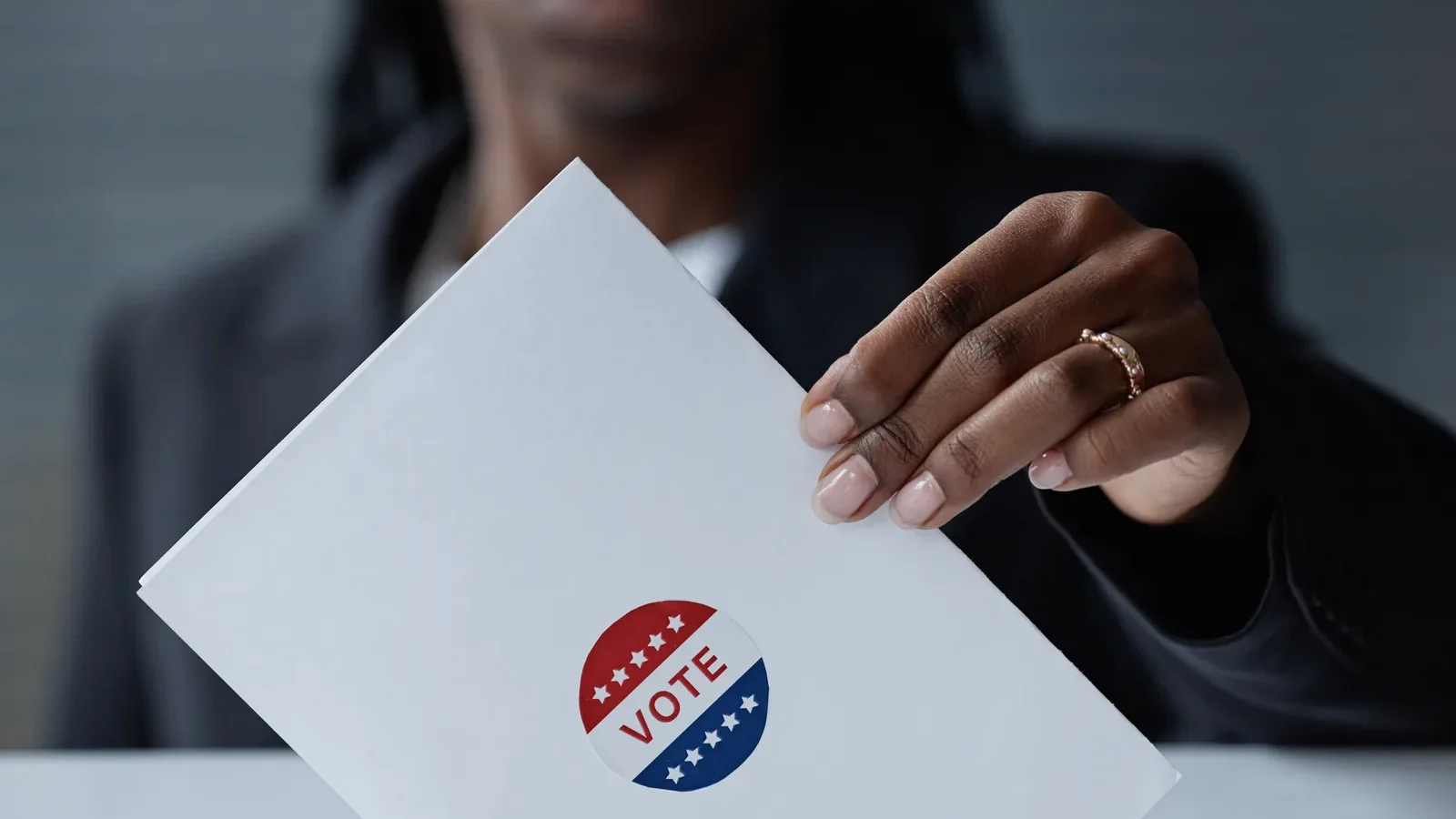 A voter holding a ballot envelope with a vote sticker over a ballot box