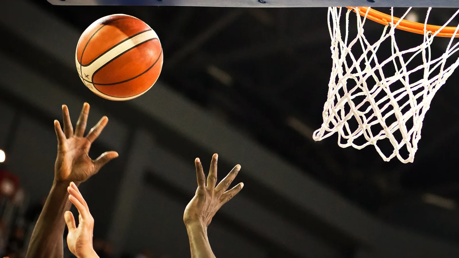 A basketball dropping toward the hoop as players reach up