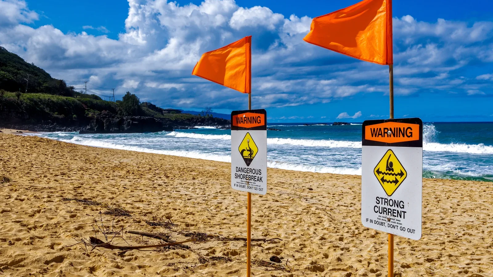 Orange flags and warning signs for shorebreak and strong current on a Hawaiʻi beach
