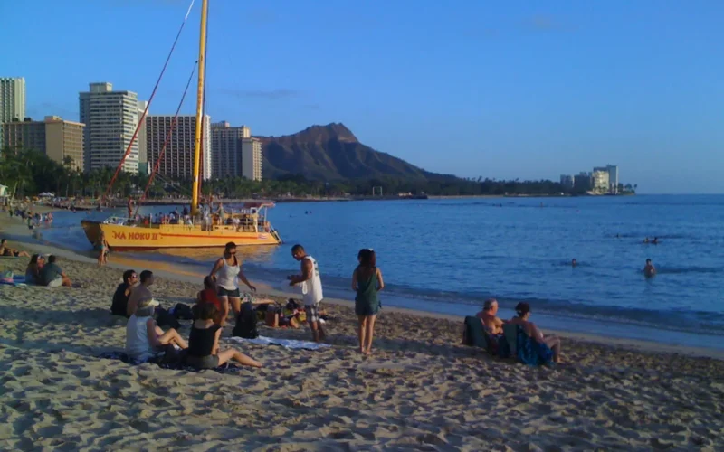 Beachgoers and a sailing catamaran on Waikīkī Beach with Diamond Head behind